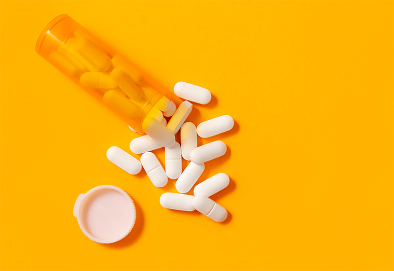 A pill bottle spilling tablets on to an orange surface