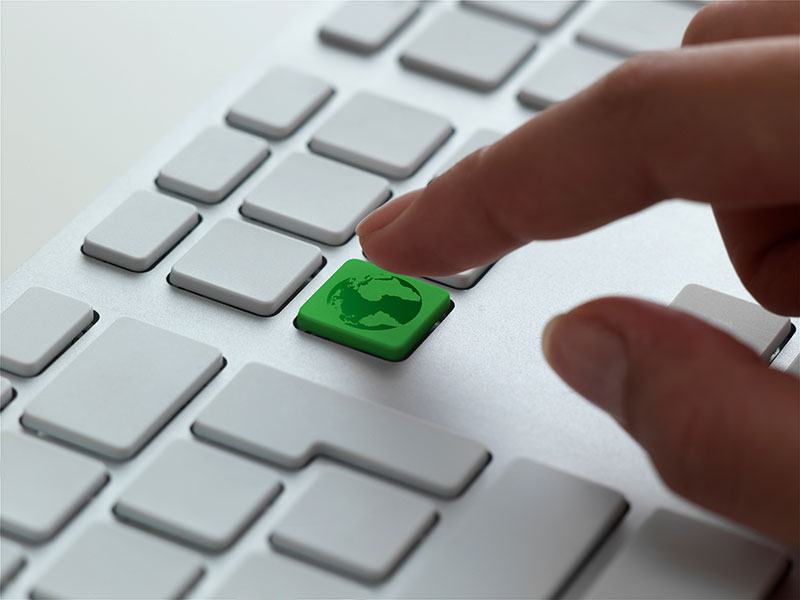 A finger pressing a green globe key on a keyboard