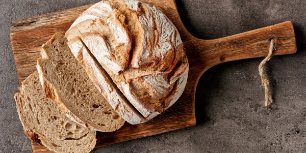 A loaf of bread made using protein enrichment ingredients, is displayed partially sliced on a cutting board.